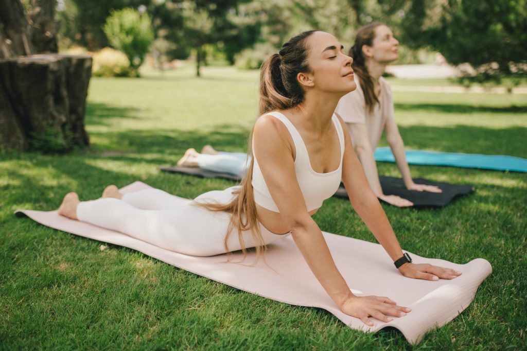Group of millennial women having group yoga class in a park. Healthy lifestyle.