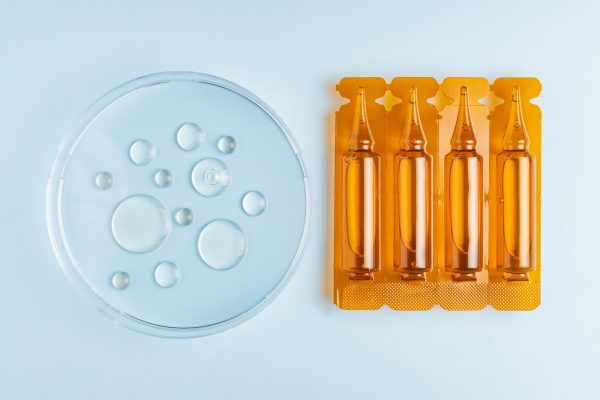 A hair care oil or serum in brown plastic ampiles or capsules on a blue background with oil samples